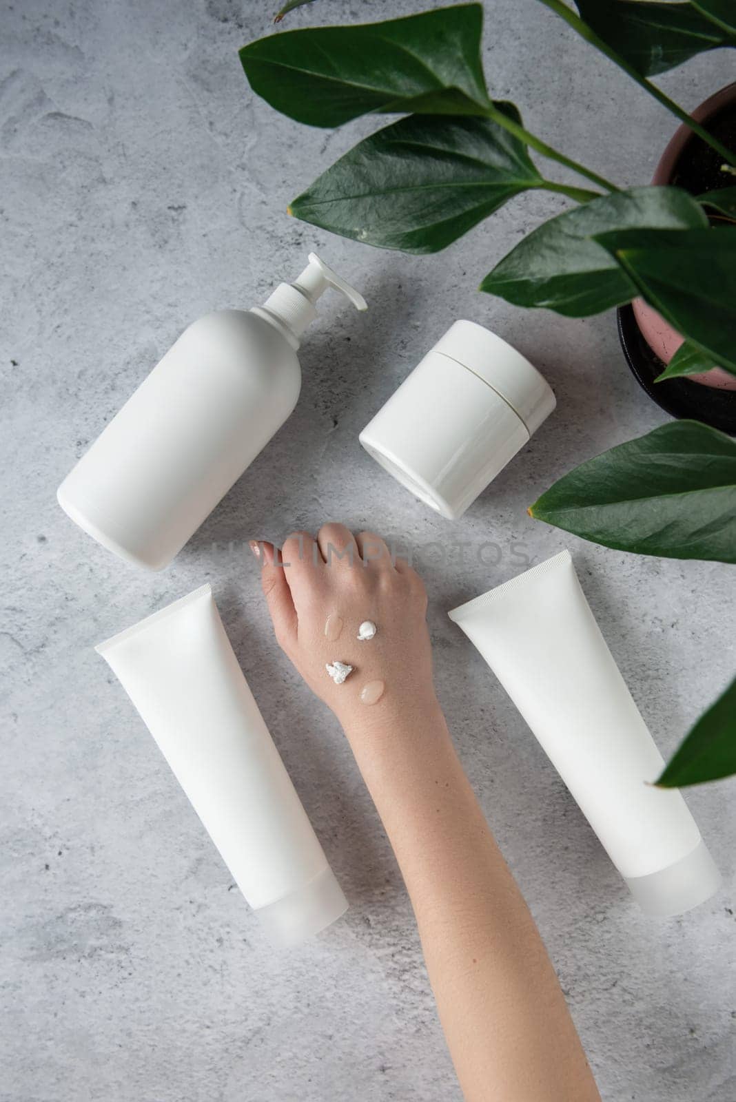 Young woman applying hand many creams at gray background