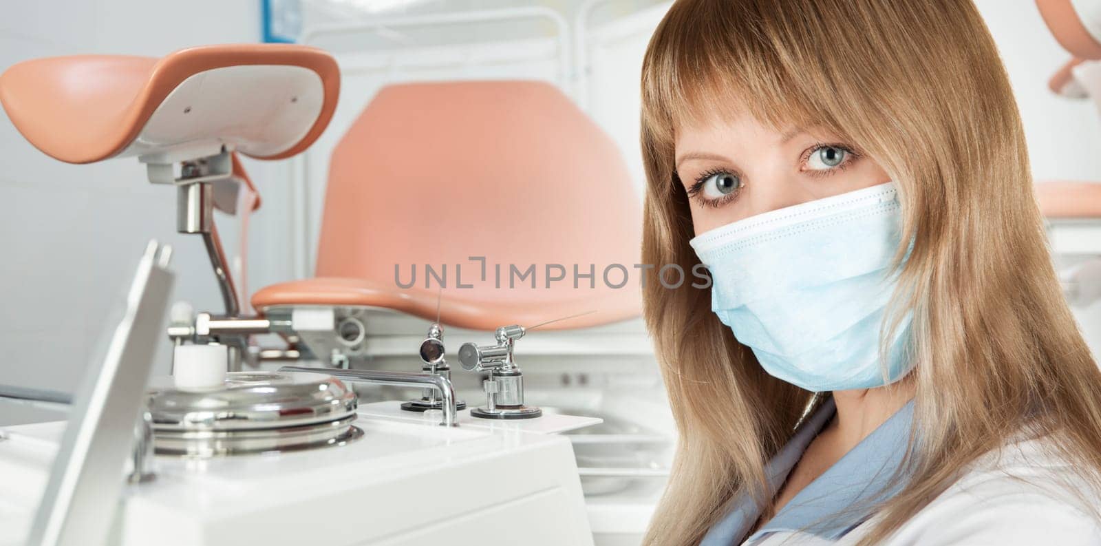 Female gynecologist in protective mask and whitecoat with gynecological vaginal retractor in hand
