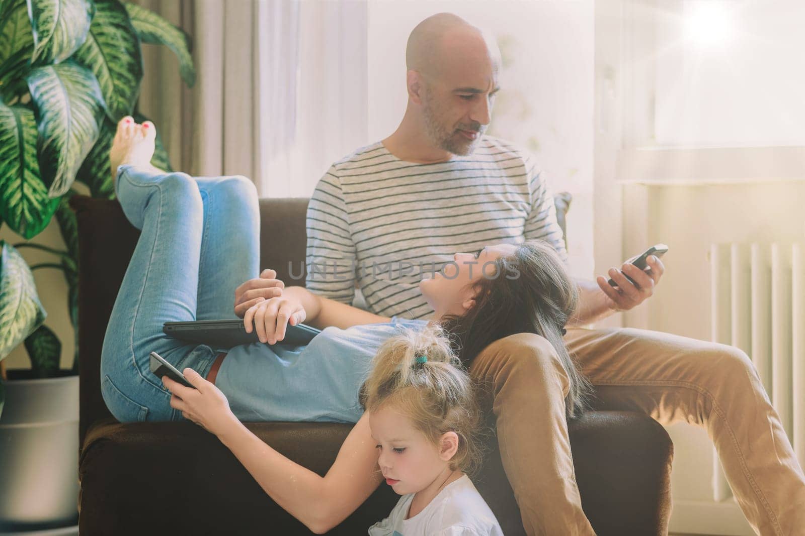 Happy family bonding over technology on the sofa at home, browsing on phones and tablets in the living room. Enjoying screen time together with smiles and love