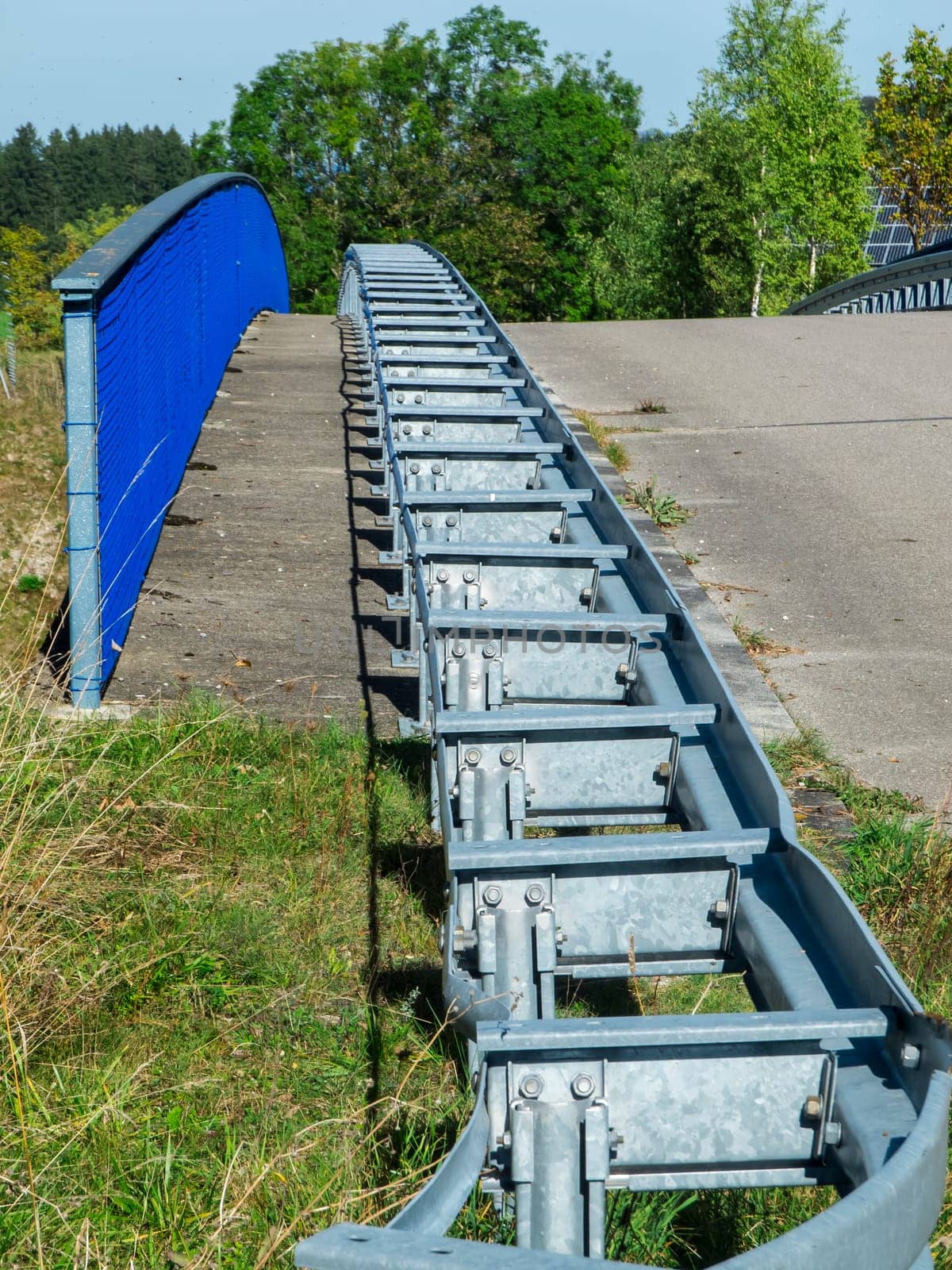 Railing with guard rails installed in front of it on a car crossing country road in summer in Bavaria.