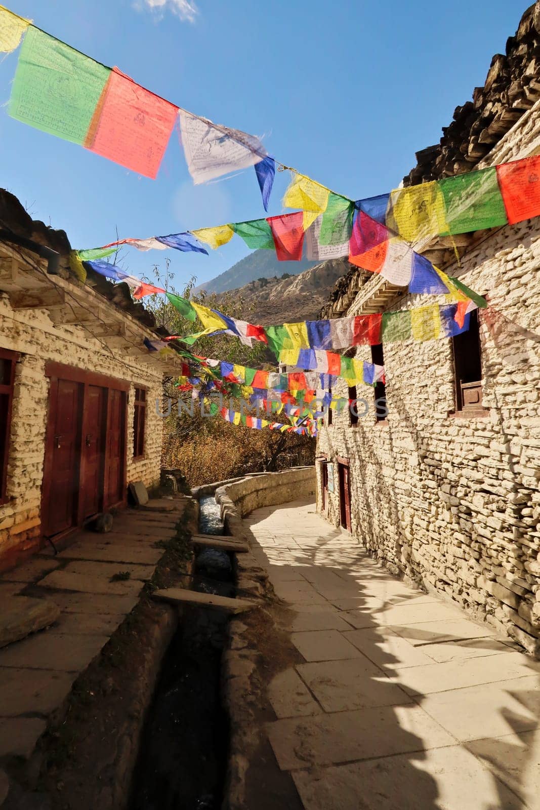 Many colorful buddhist prayer flags between traditional stone houses in the remote mountain village of Marpha, Annapurna Circuit Trek, Nepal 2022