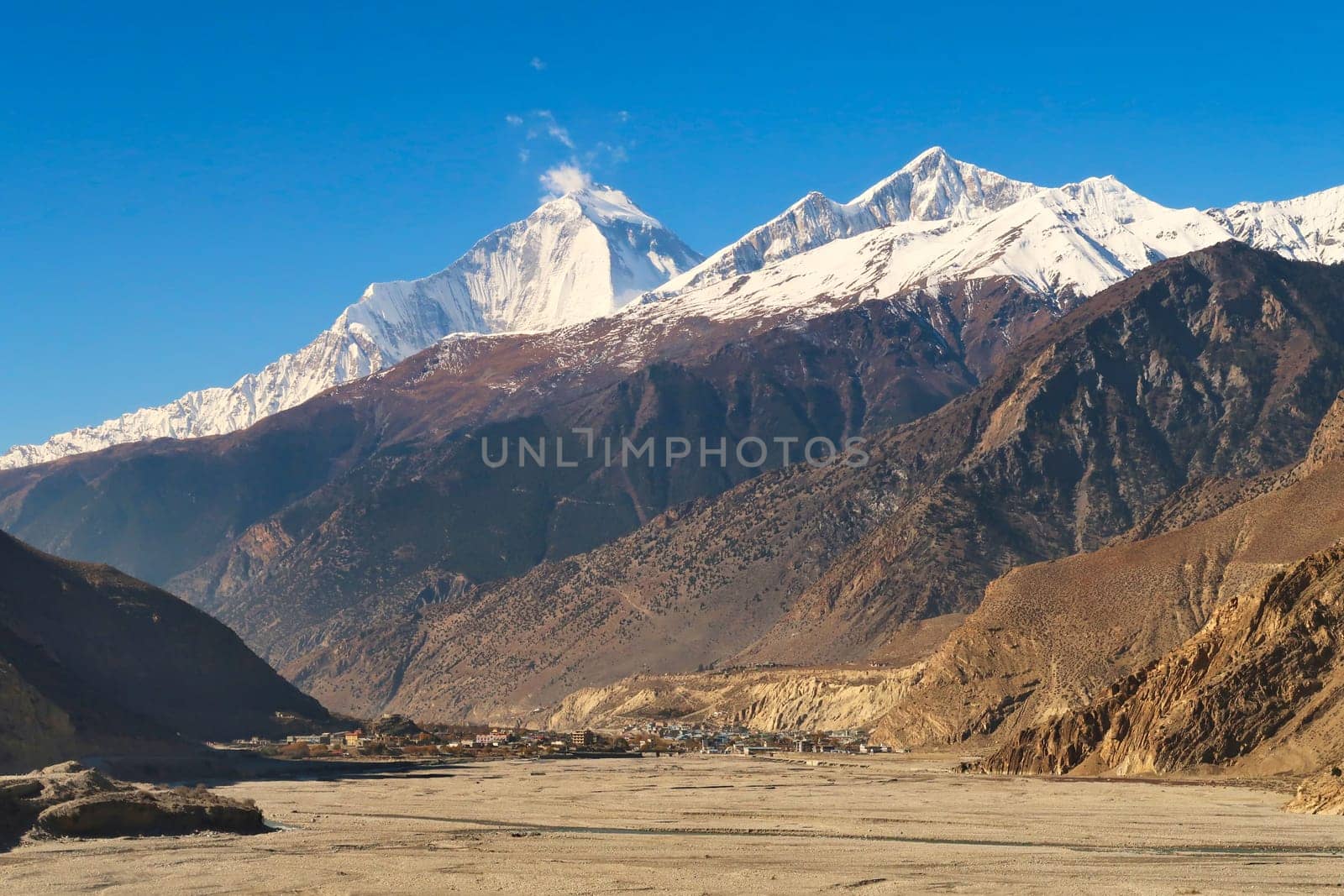 The town, village of Jomsom behind the dried up riverbed of the Kali Gandaki River, the snow capped peak of Mount Dhaulagiri I rises in the background, Annapurna Circuit Trek, Nepal 2022