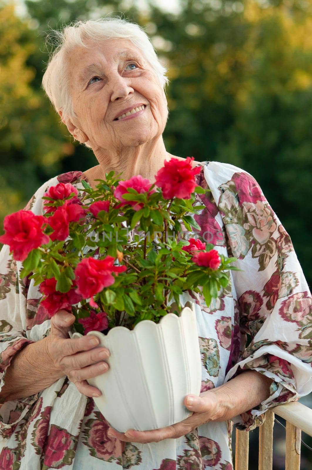 The senior old woman with flowers on the balcony at home