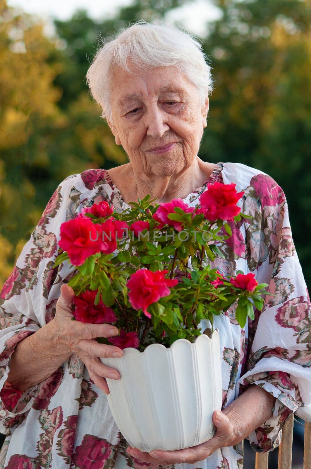 The senior old woman with flowers on the balcony at home