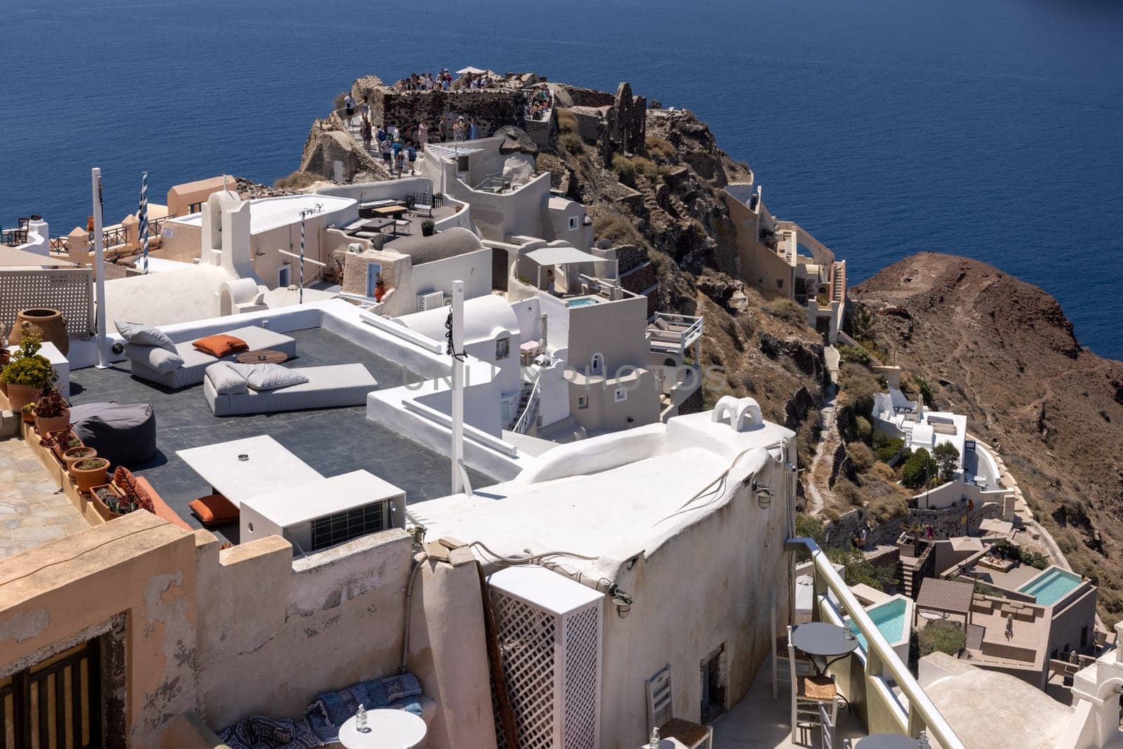 Oia, Santorini, Greece - July 3, 2021: Whitewashed buildings and the ruins of Castle of Agios Nikolaos on the edge of the caldera cliff, Oia village, Santorini, Greece