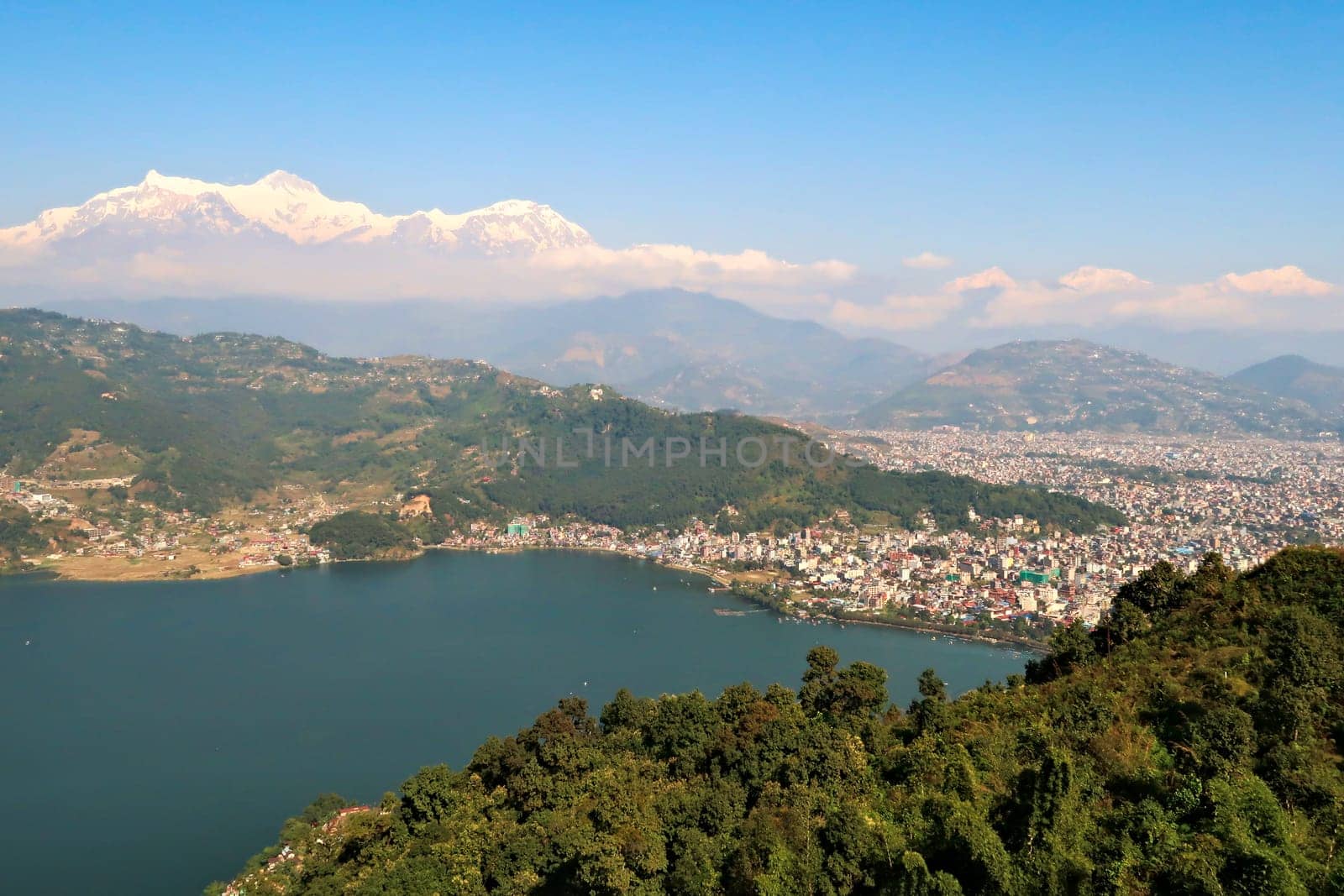 View onto the town of Pokhara at the shore of Phewa Lake, a mountain range with Mount Machapuchare on the left rising in the back, on the way up to the World Peace Pagoda, Nepal 2022