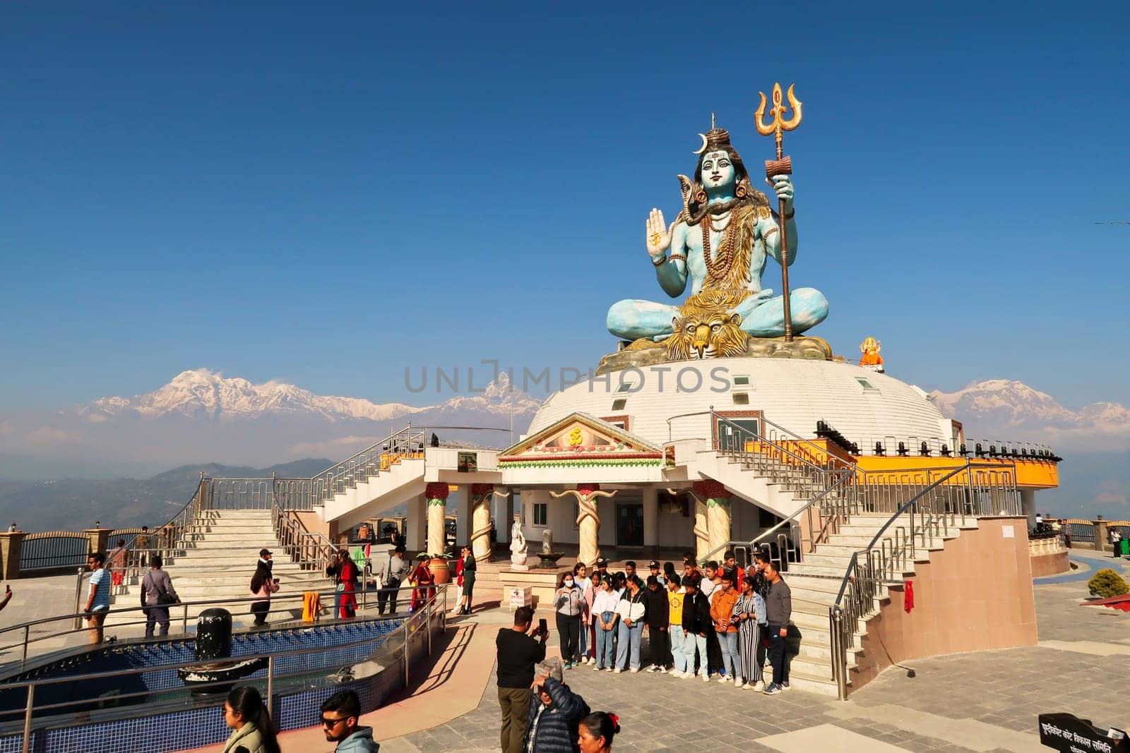 People gather at the statue of Shiva at the Pumdikot Religious Area in front of a mountain range with Mount Machapuchare in the middle, close to Phewa Lake, Pokhara, Nepal 2022