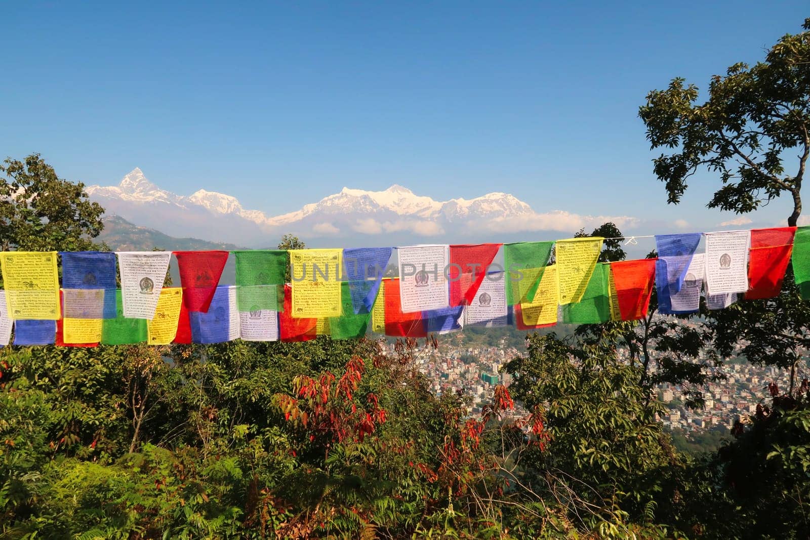 View onto the mountains rising behind the Phewa Lake, Machapuchare on the left, colorful prayer flags in the foreground, on the way up to the World Peace Pagoda, Pokhara, Nepal 2022