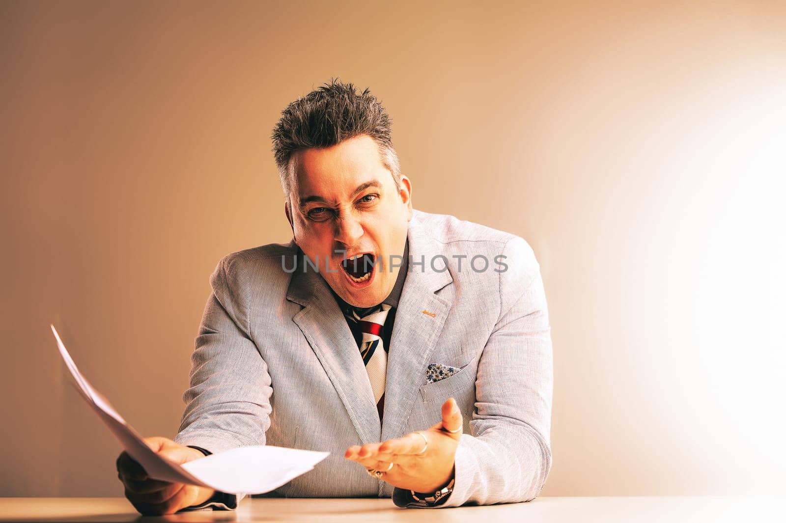 Businessman is experiencing extreme frustration, holding papers and shouting with his mouth wide open, conveying workplace stress and anger