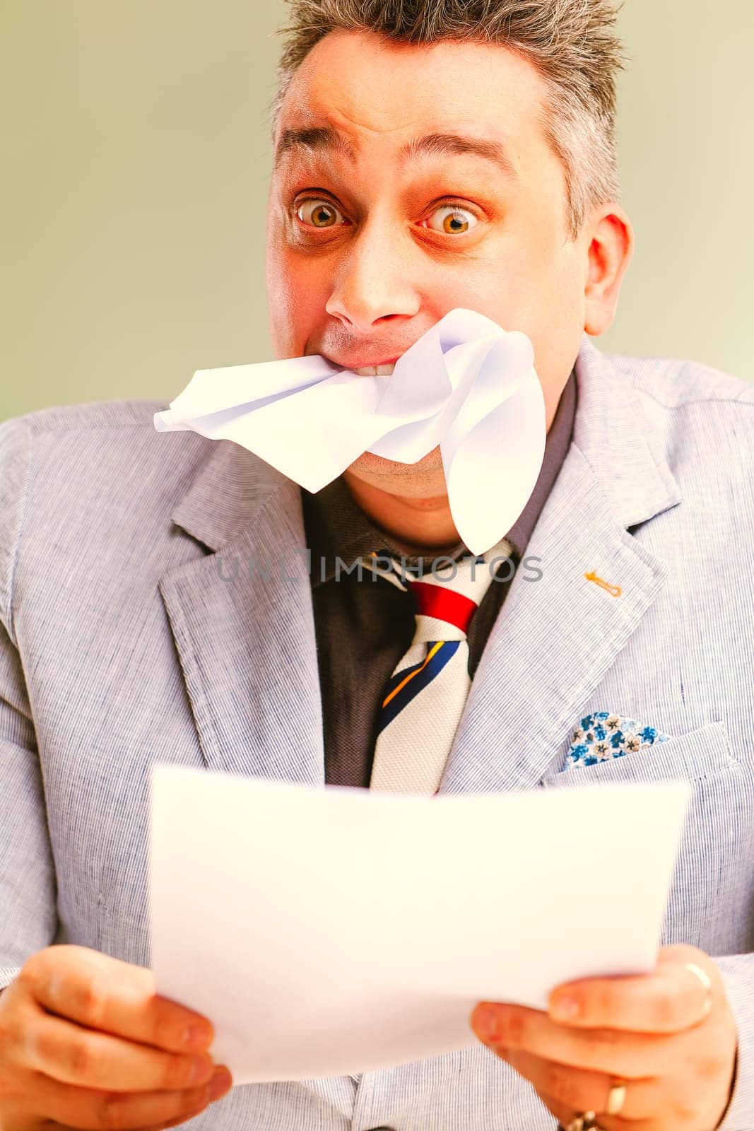 Overwhelmed businessman biting paper, shocked and worried, facing stress and burnout in corporate setting. Irony and satire of workplace emotions