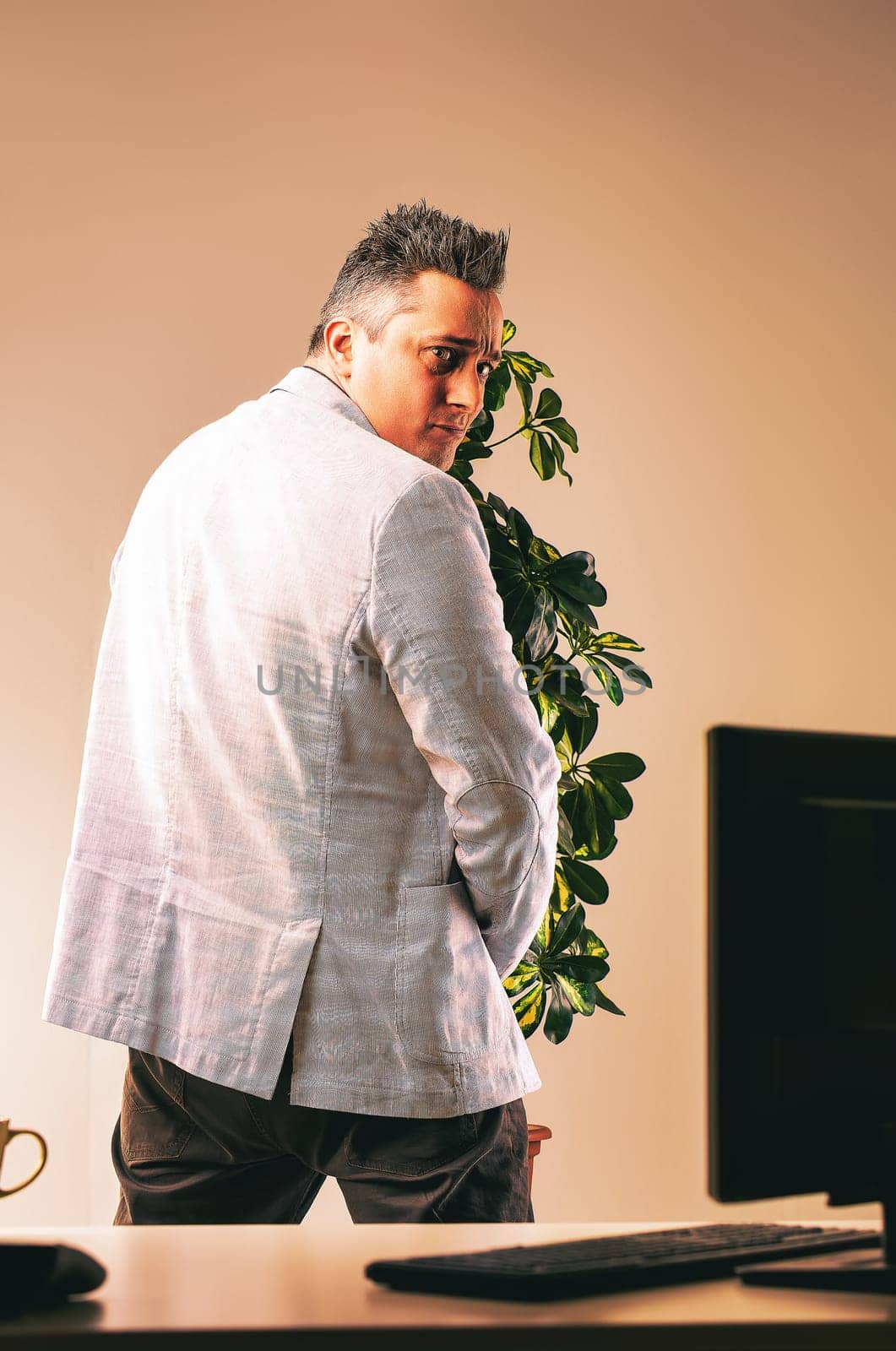 Manager hides behind a plant, peeking over his shoulder with a sneaky expression in an office, creating a negative workplace atmosphere
