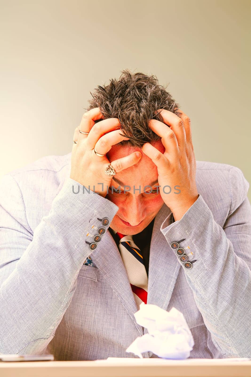 Businessman is suffering from a strong headache and feeling stressed while sitting at his desk with a crumpled piece of paper in front of him