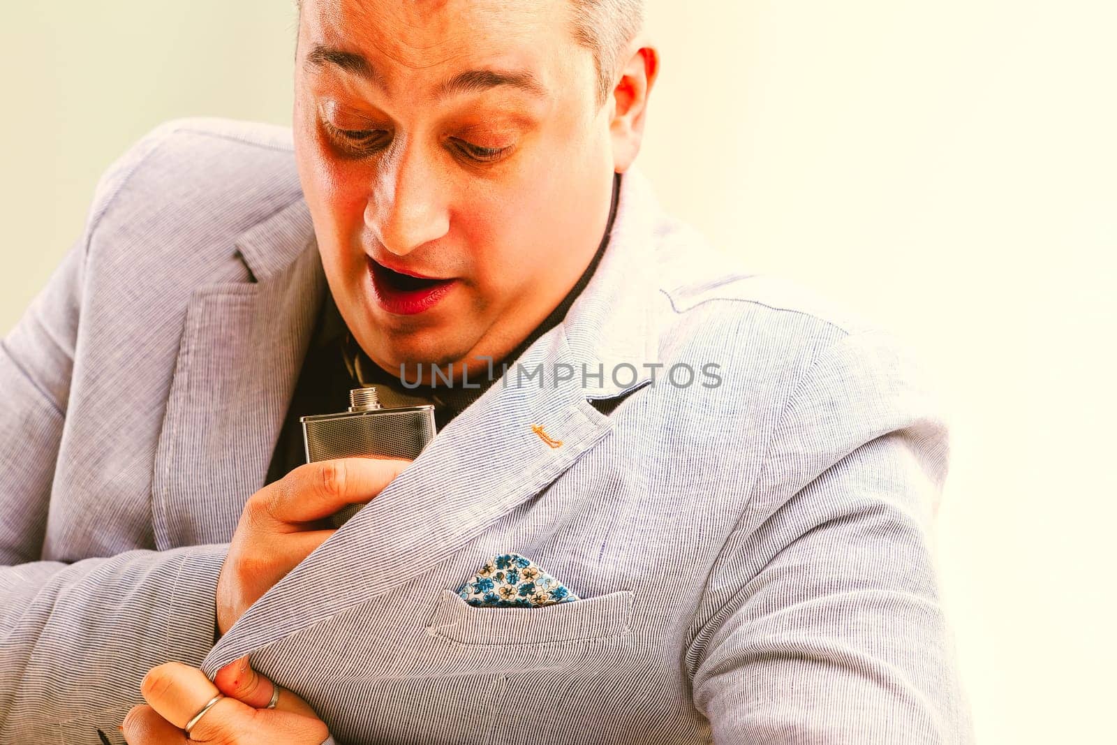 Overwhelmed mature businessman smelling a perfume bottle inside his jacket pocket. Concept of funny and unexpected fragrance reaction