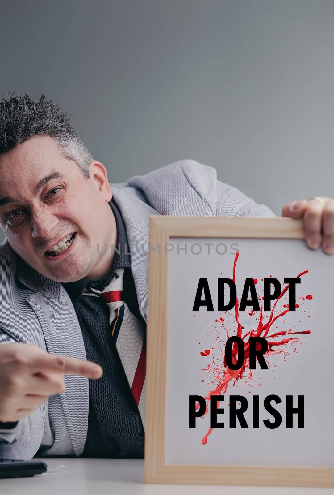 Businessman is pointing at a sign that says adapt or perish with a determined expression, emphasizing the need for adaptation in a competitive business environment
