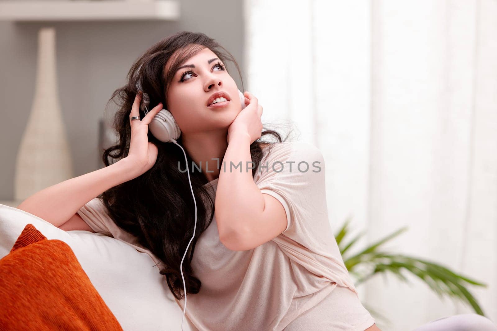 Young woman lounges on her cozy sofa at home, listening to music with headphones, looking happy and serene
