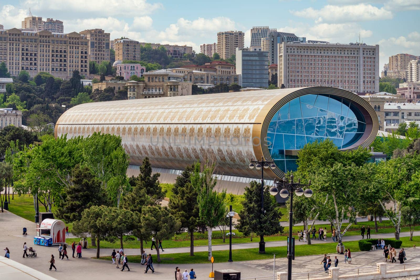 Baku, Azerbaijan - May 5, 2024: Visitors explore the unique architecture and exhibits of the Carpet Museum in Baku, surrounded by greenery and city life.