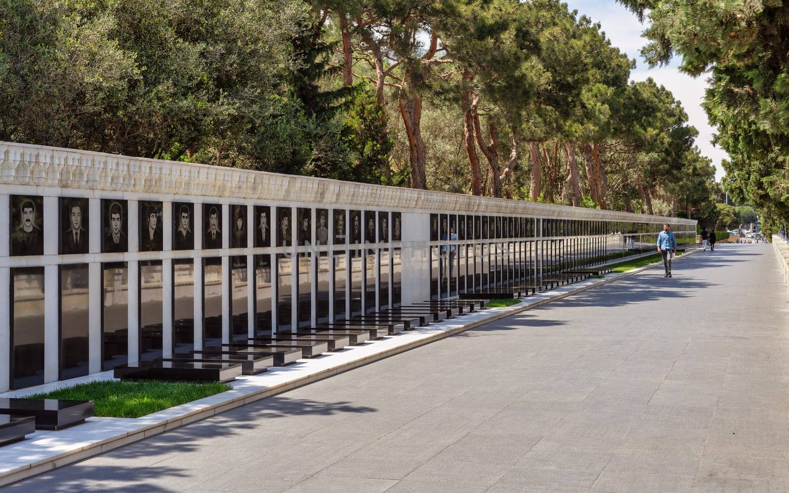 Baku, Azerbaijan - May 6, 2024: Few visitors stroll along Martyrs' Lane, observing memorial portraits amidst verdant trees and a serene atmosphere