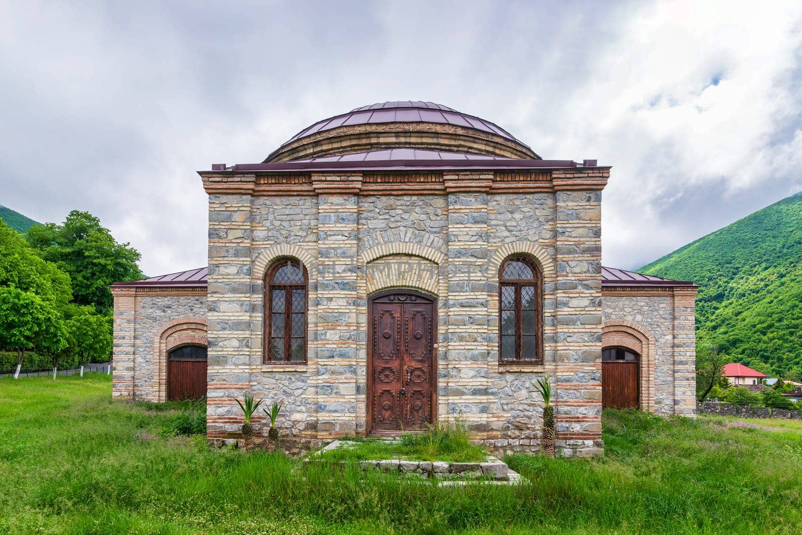 Three Saints Church, or the Round Temple, stands surrounded by lush greenery and mountains in Shaki, Azerbaijan