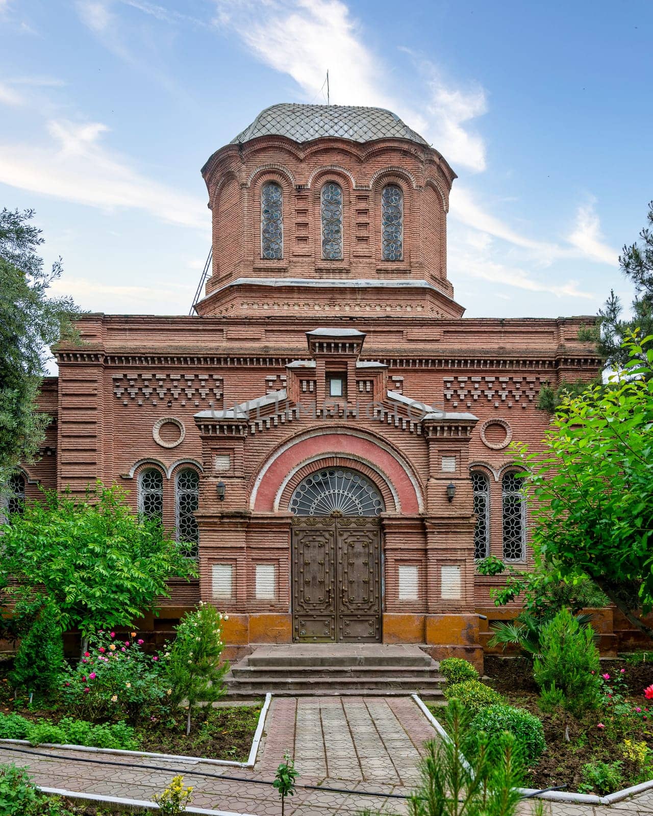 A stunning view of Alexander Nevsky Church showcases its intricate red bricks architecture amidst vibrant gardens in Ganja, Azerbaijan