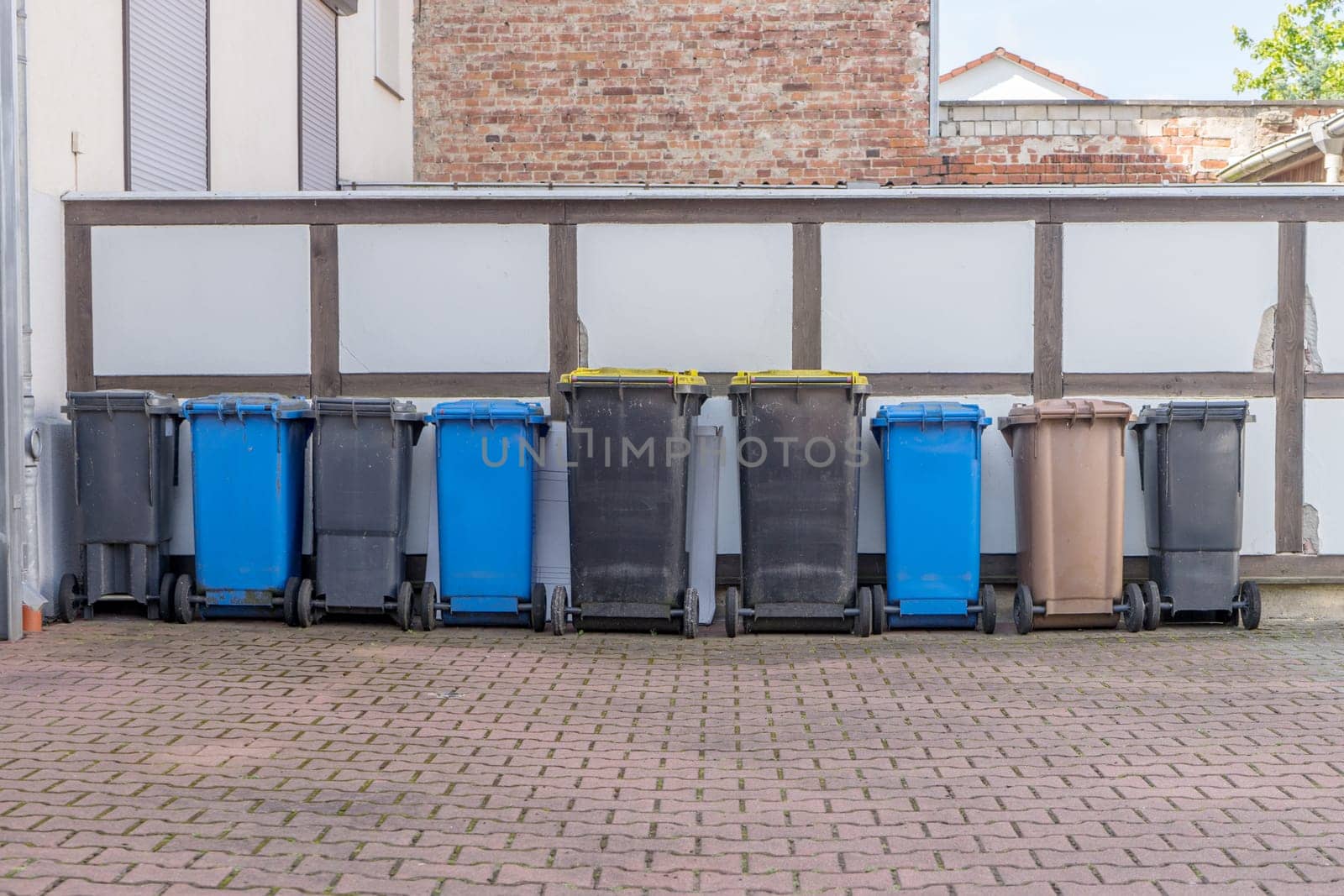 Row of gray, brown and blue garbage cans in front of a wall