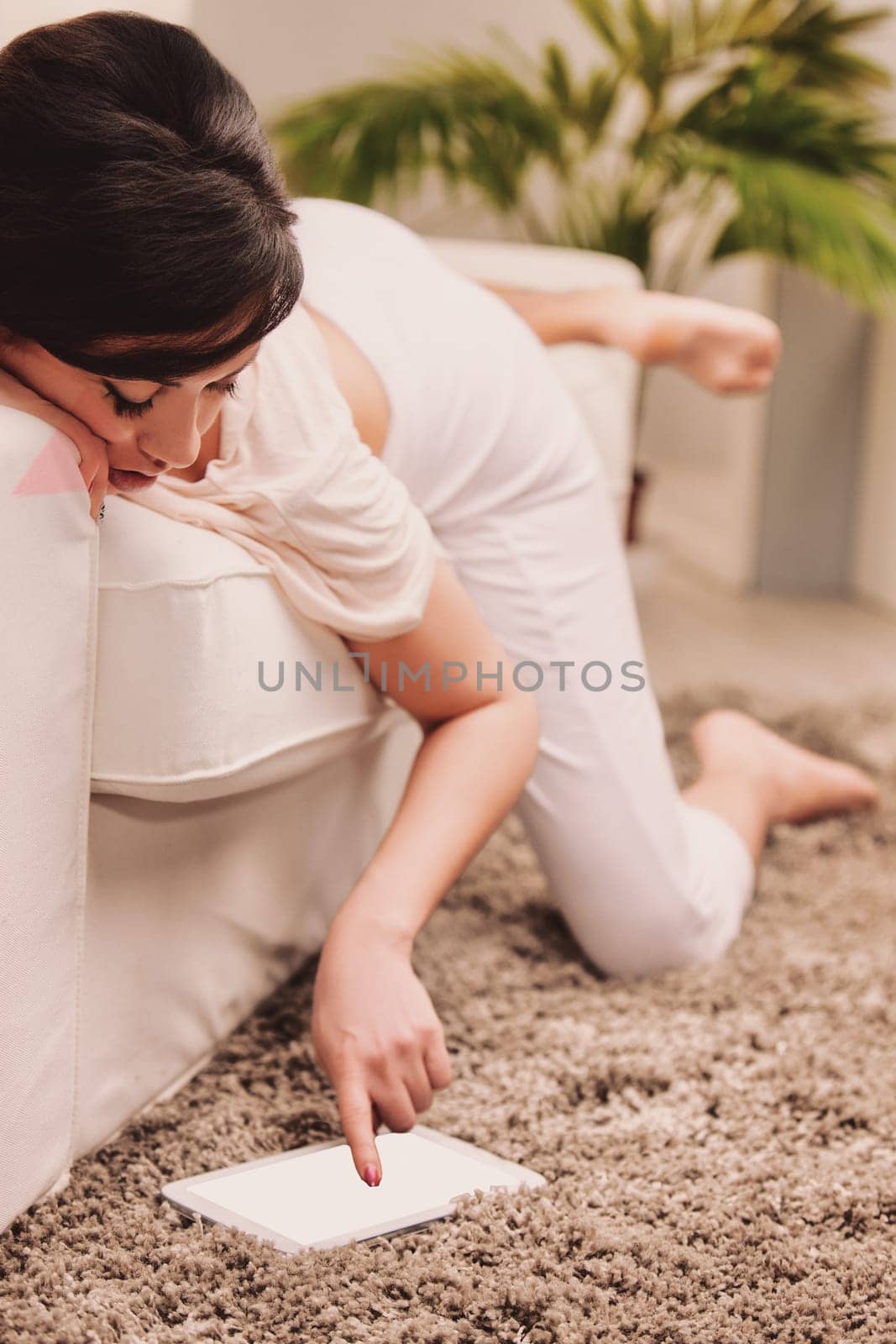 Lifestyle A young woman is enjoying her leisure time while relaxing on a comfortable sofa, browsing on a digital tablet