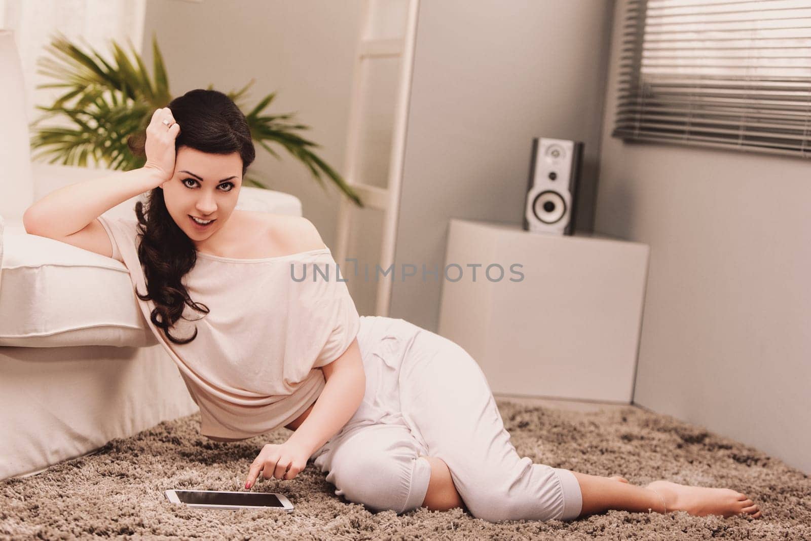 Lifestyle Young woman lying on the carpet in her living room, using a digital tablet and enjoying her free time