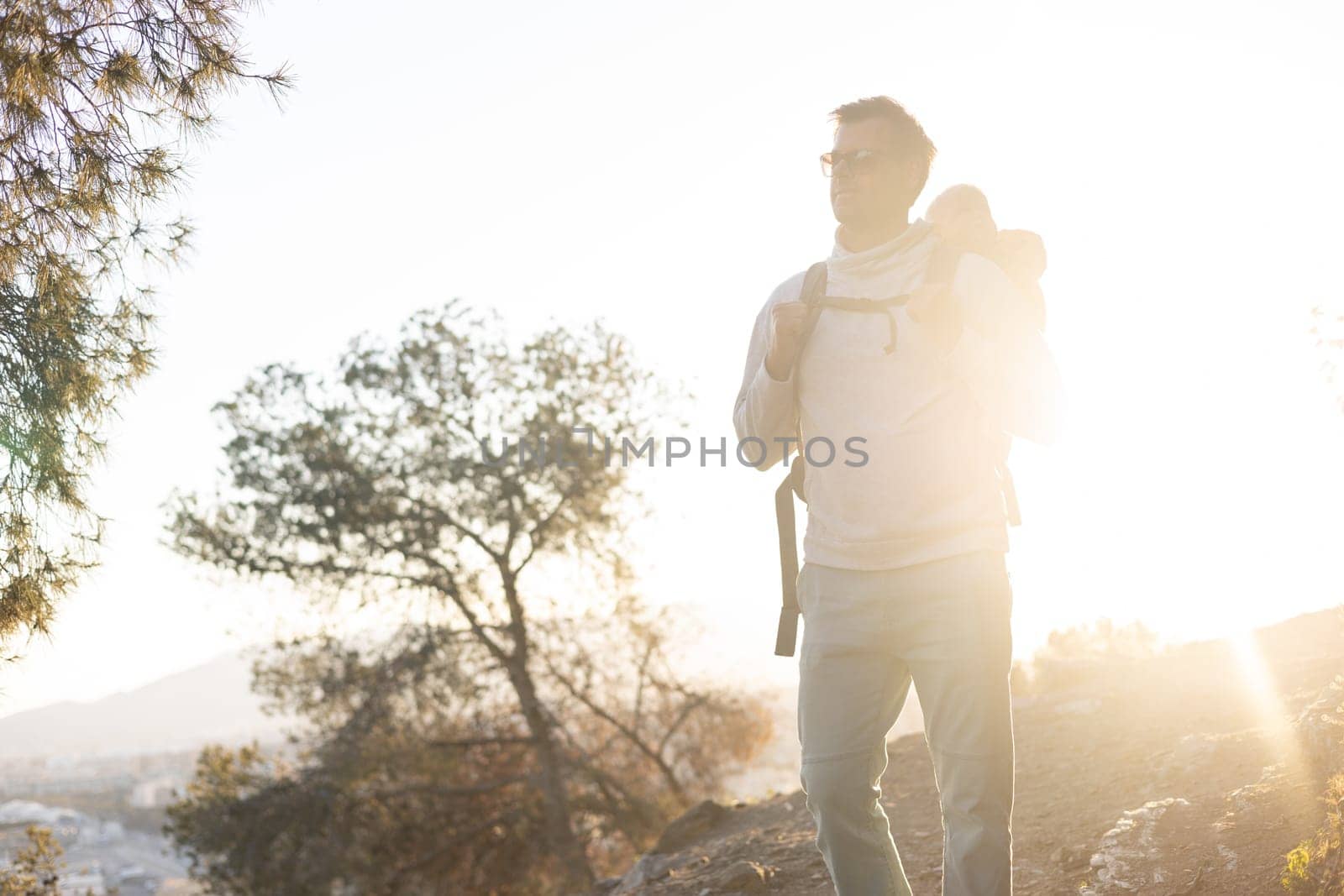 Young father carrying his infant baby boy son in backpack while tracking around Malaga, Spain in sunset. Family travel and vacation concept.