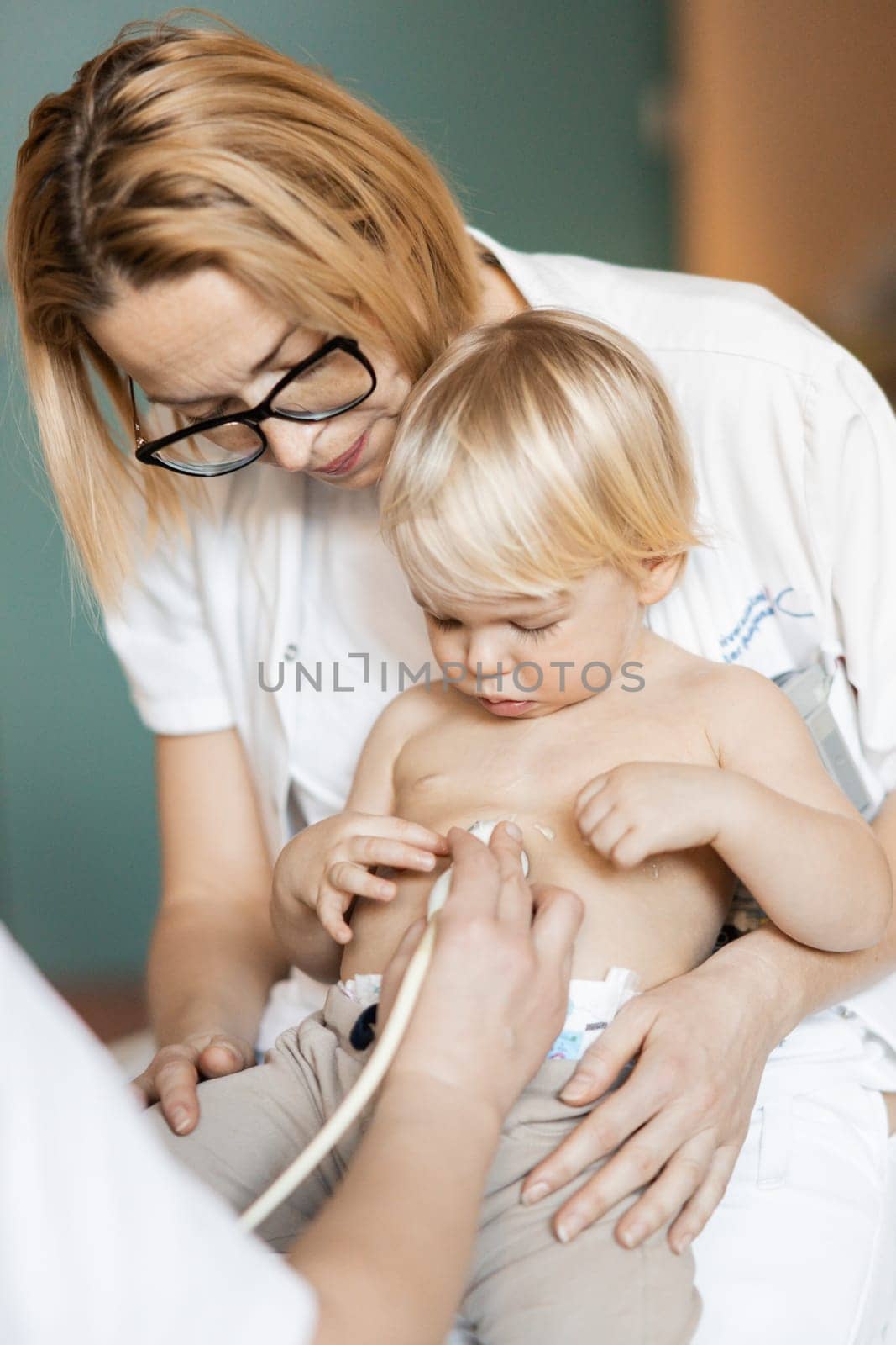 Small child being checked for heart murmur by heart ultrasound exam by cardiologist as part of regular medical checkout at pediatrician
