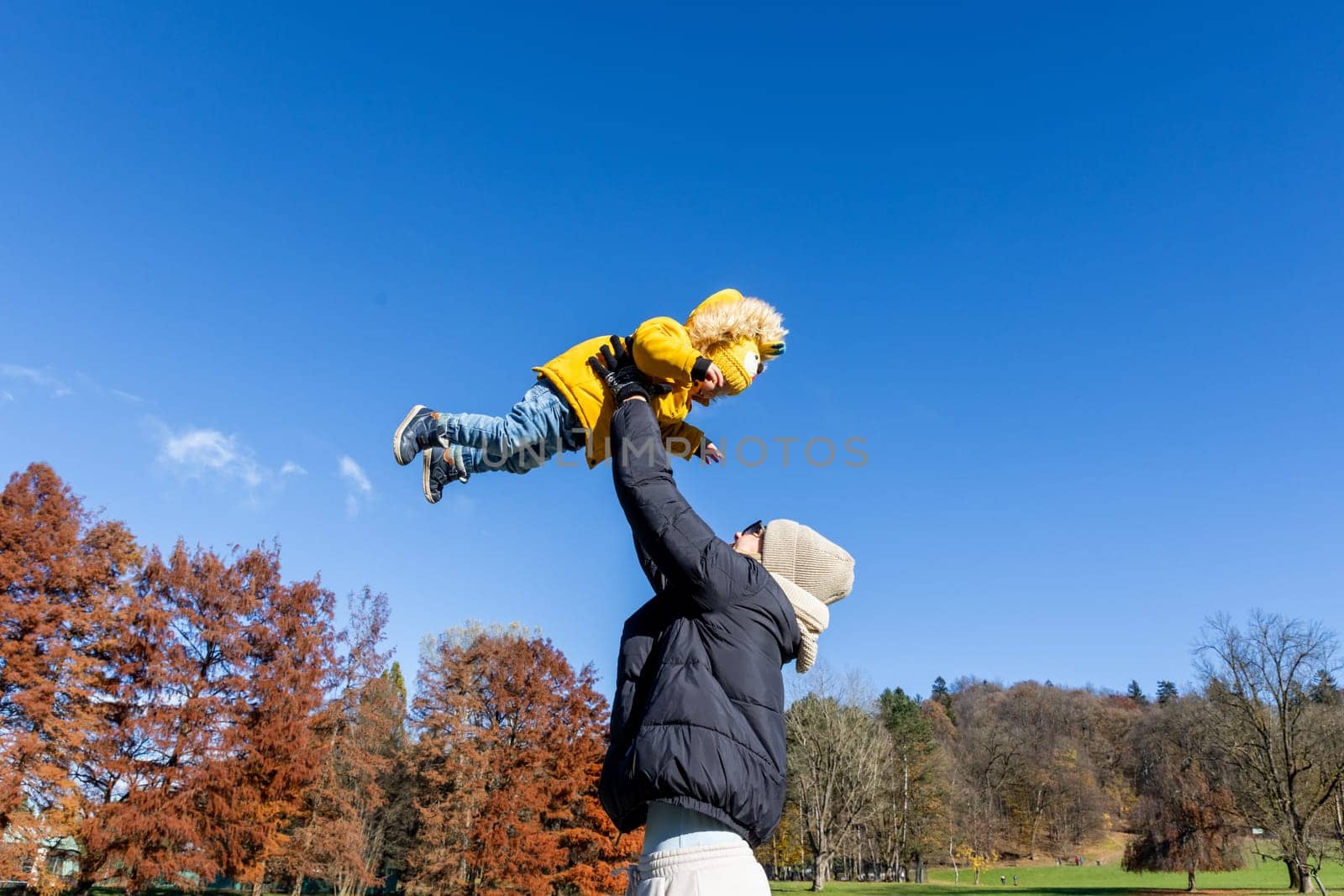More, more,...mum, that's fun. Happy young mother throws her cute little baby boy up in the air. Mother's Day, Mather and her son baby boy playing and hugging outdoors in nature in fall