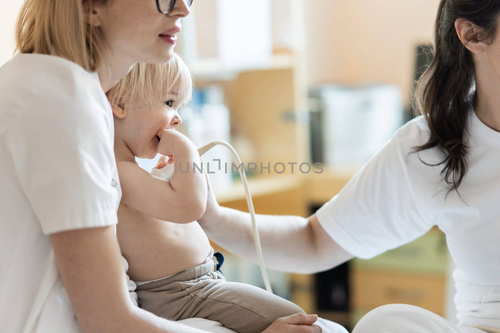 Small child being checked for heart murmur by heart ultrasound exam by cardiologist as part of regular medical checkout at pediatrician