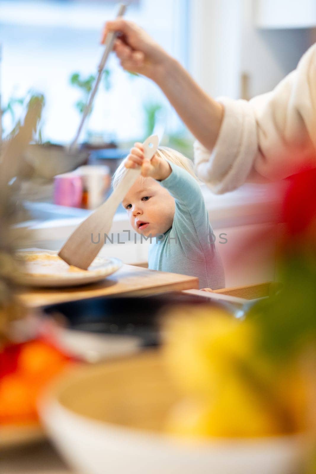 Mother and little toddler baby boy making pancakes for breakfast together in domestic kitchen. Family, lifestyle, domestic life, food, healthy eating and people concept