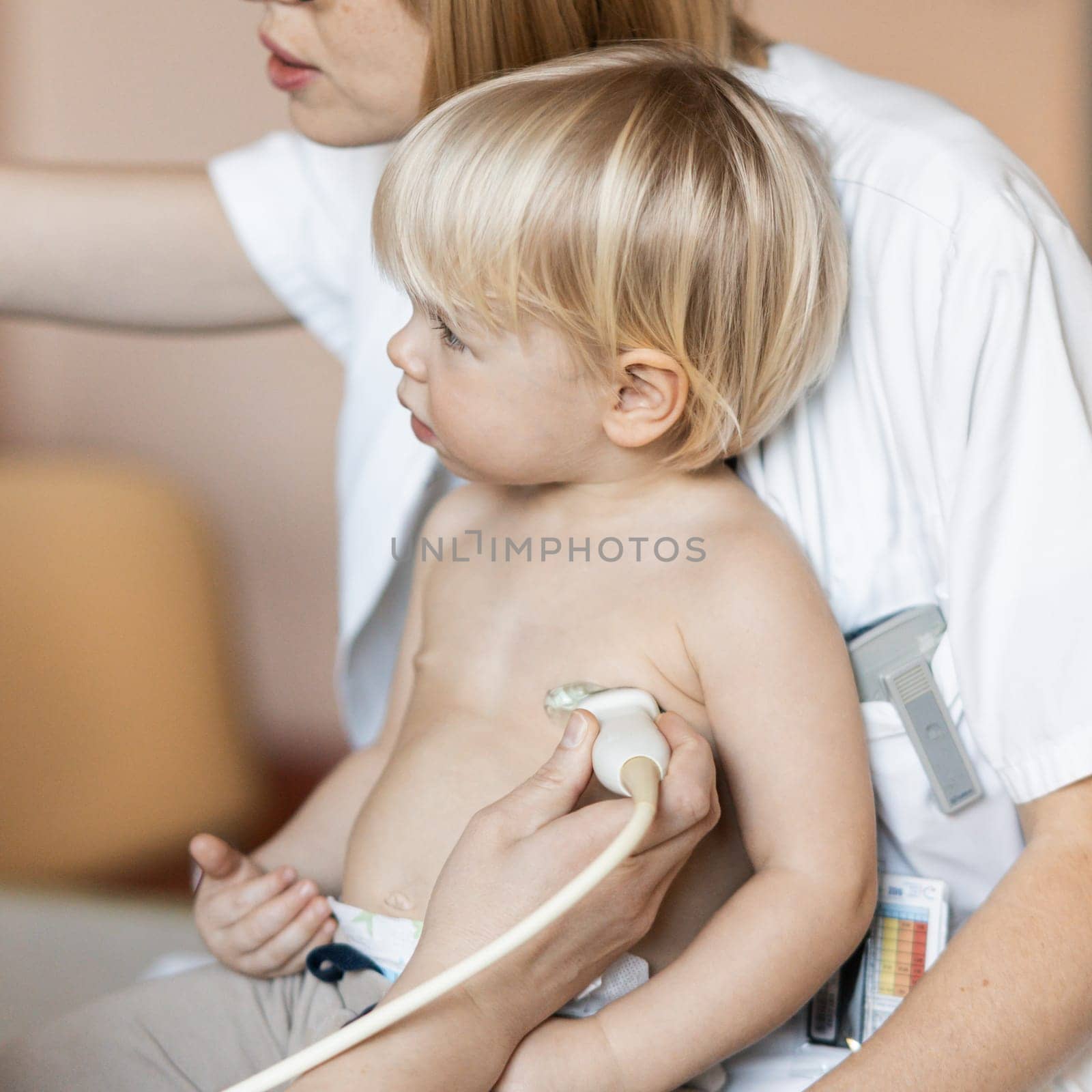 Small child being checked for heart murmur by heart ultrasound exam by cardiologist as part of regular medical checkout at pediatrician