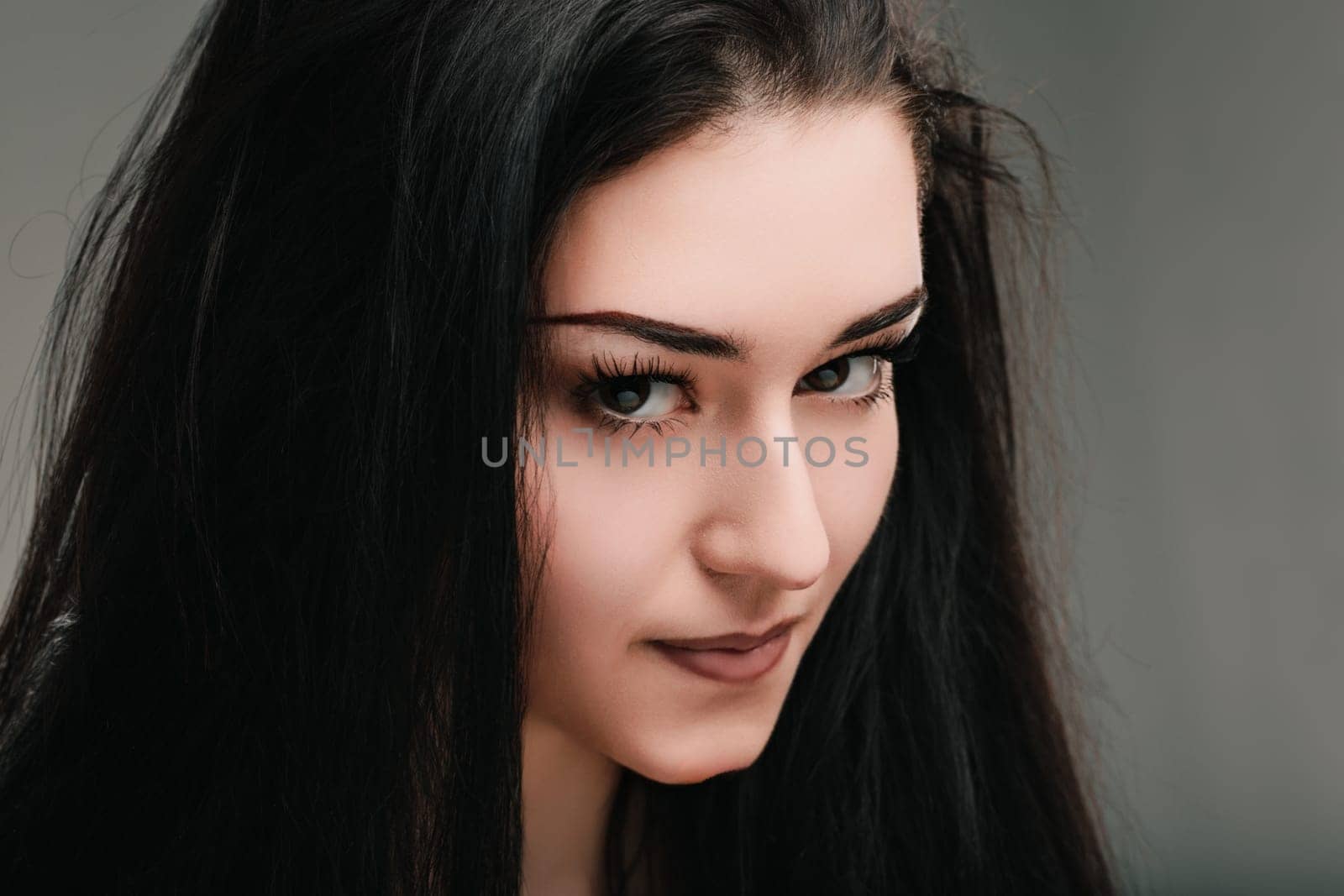 Youthful woman with dark hair is posing in front of a gray background, her expression suggesting deep thought and introspection