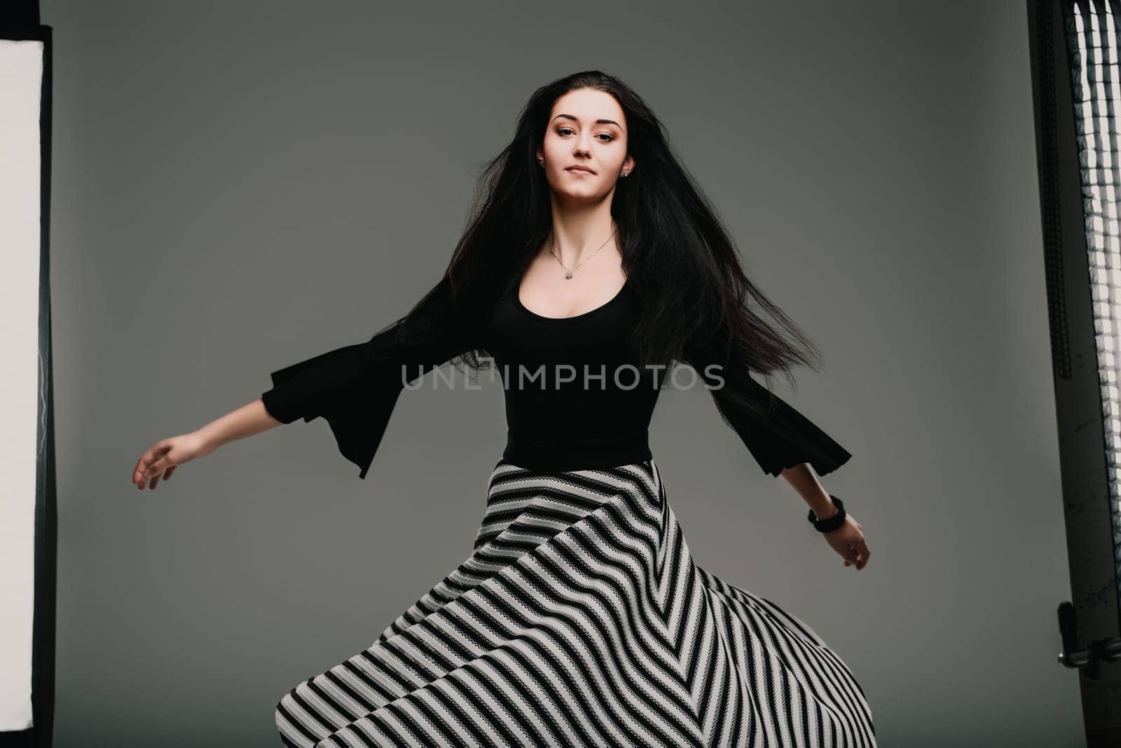 Young woman is spinning gracefully in a studio, her striped skirt flowing around her. She is wearing a black top and has long, dark hair