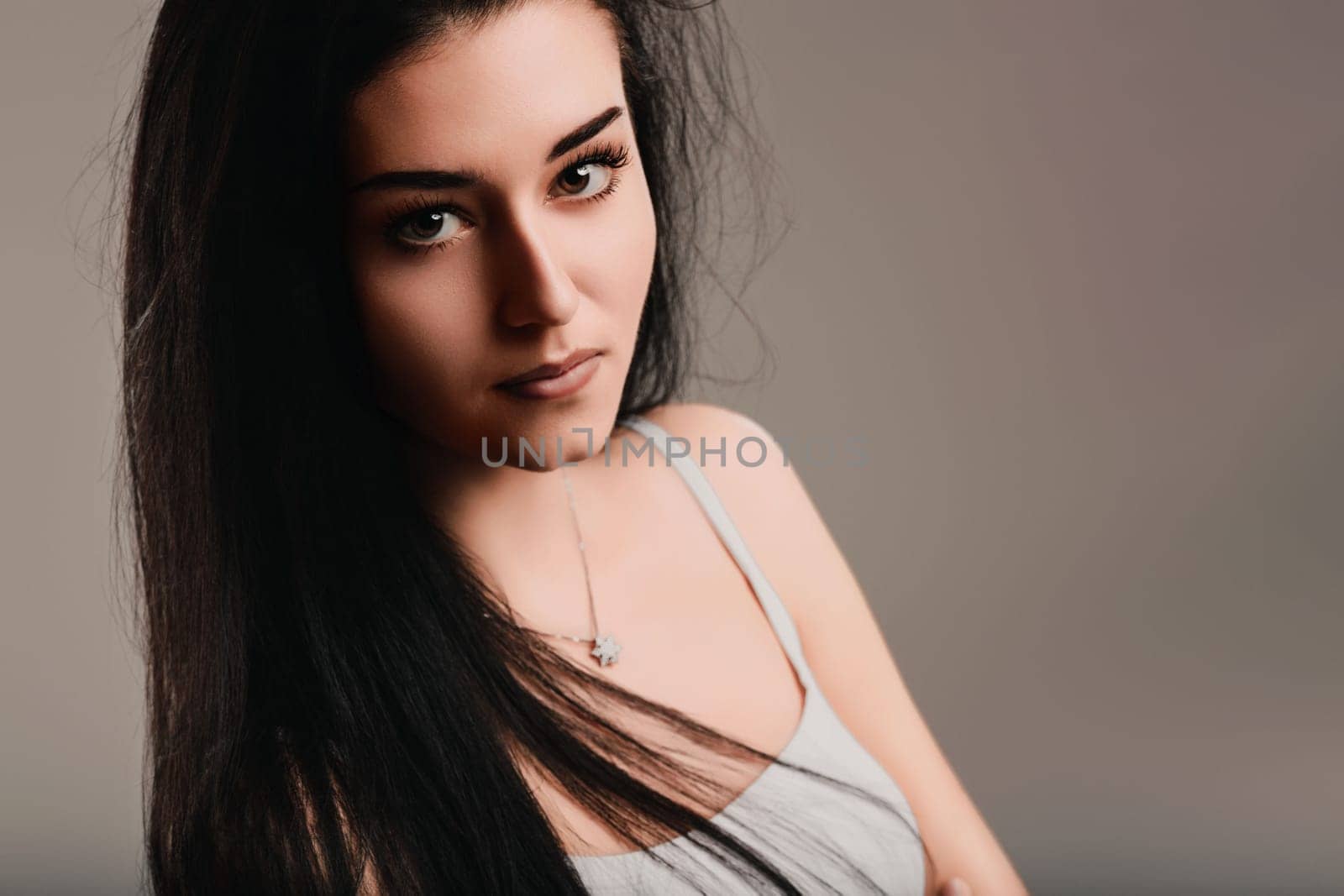Young woman with long black hair is posing in front of a muted background, her serious expression suggesting deep thought and contemplation