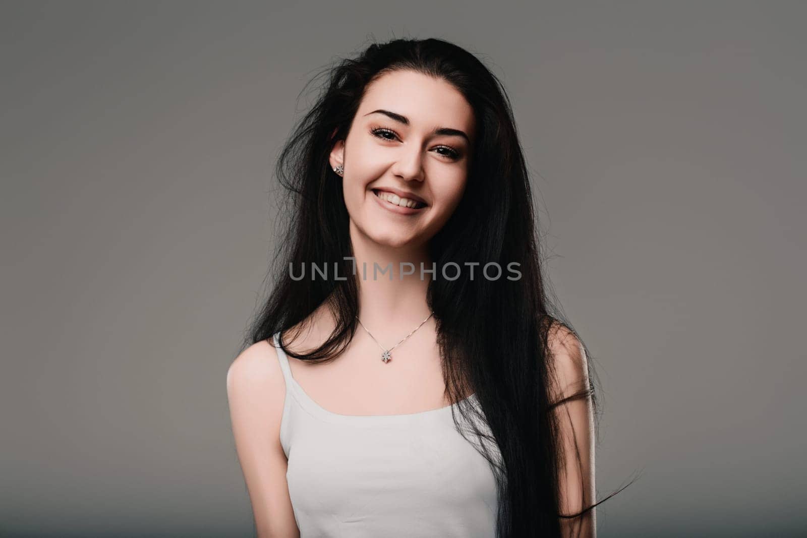 Young woman with long dark hair is smiling while lost in thought. Her pleasant expression suggests a positive and contemplative mood