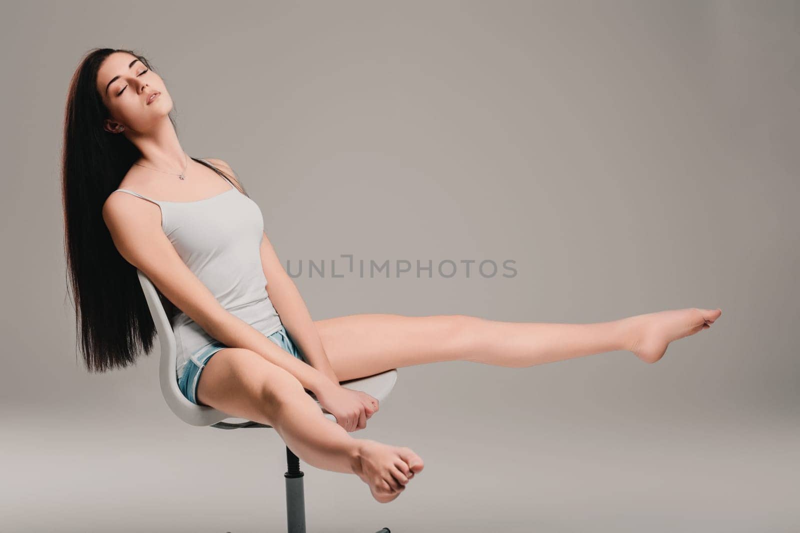Young woman with long dark hair relaxes on a chair, eyes closed in peaceful meditation. She exudes calm and tranquility, lost in thought