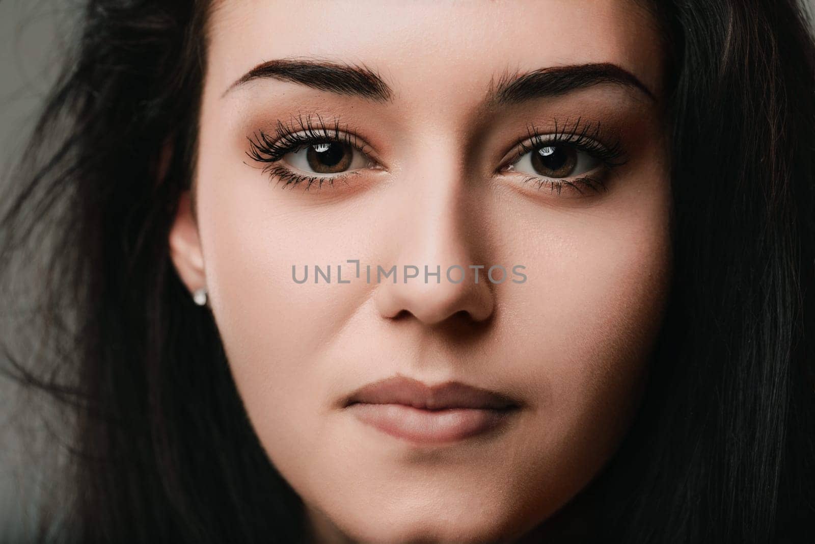 Close up of a young woman with brown eyes and long dark hair, her neutral expression hinting at a moment of quiet reflection