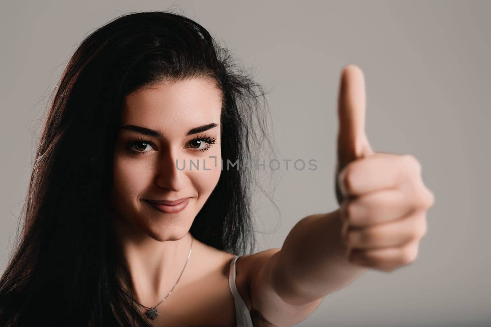 Young woman is showing a thumbs up gesture while smiling slightly, expressing a sense of consideration and reflection