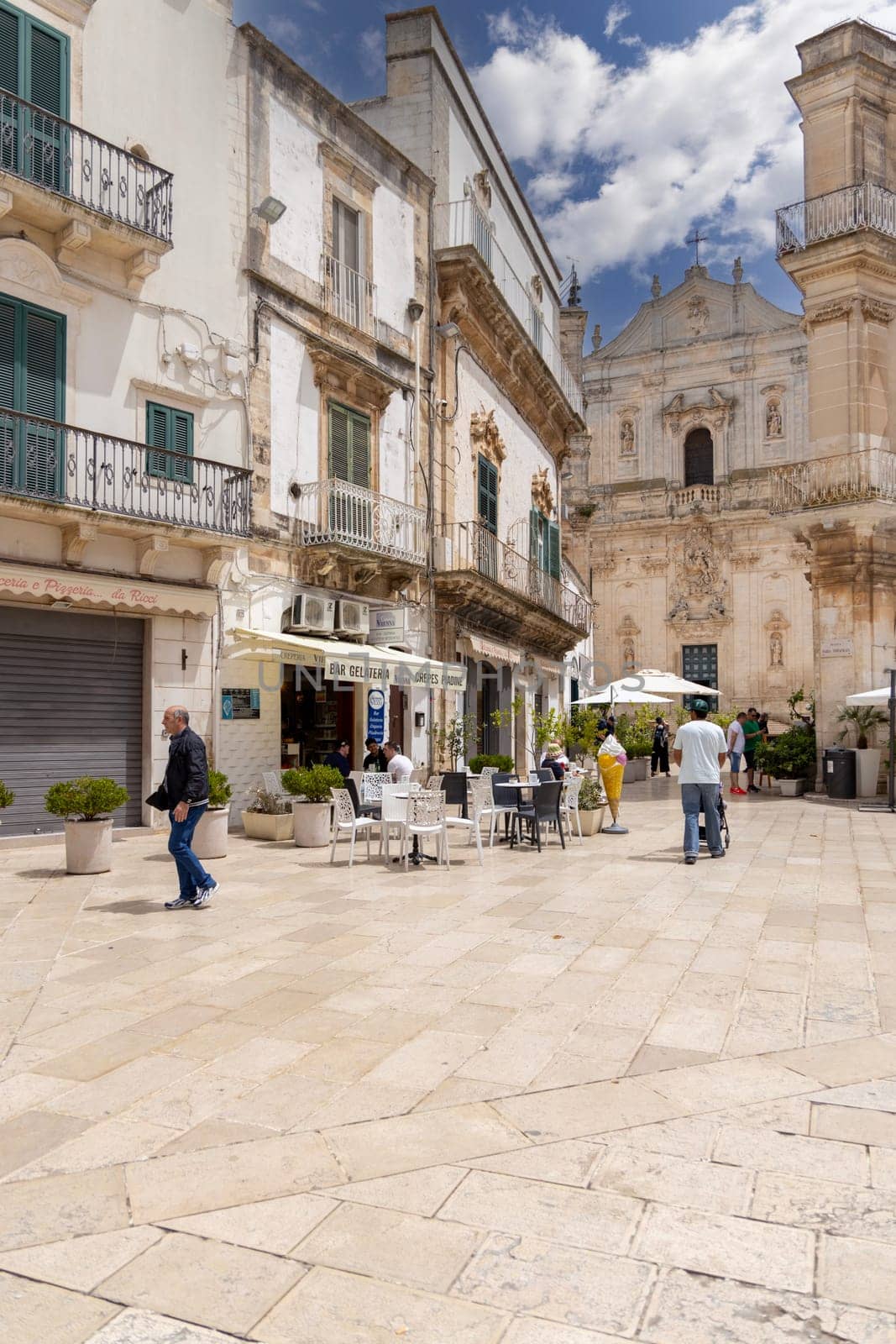Martina Franca, Italy, Apulia - May 25, 2024:  Maria Immaculate Square (Piazza Maria Immacolata), historical portici in neoclassical style. Basilica of San Martino in a distance