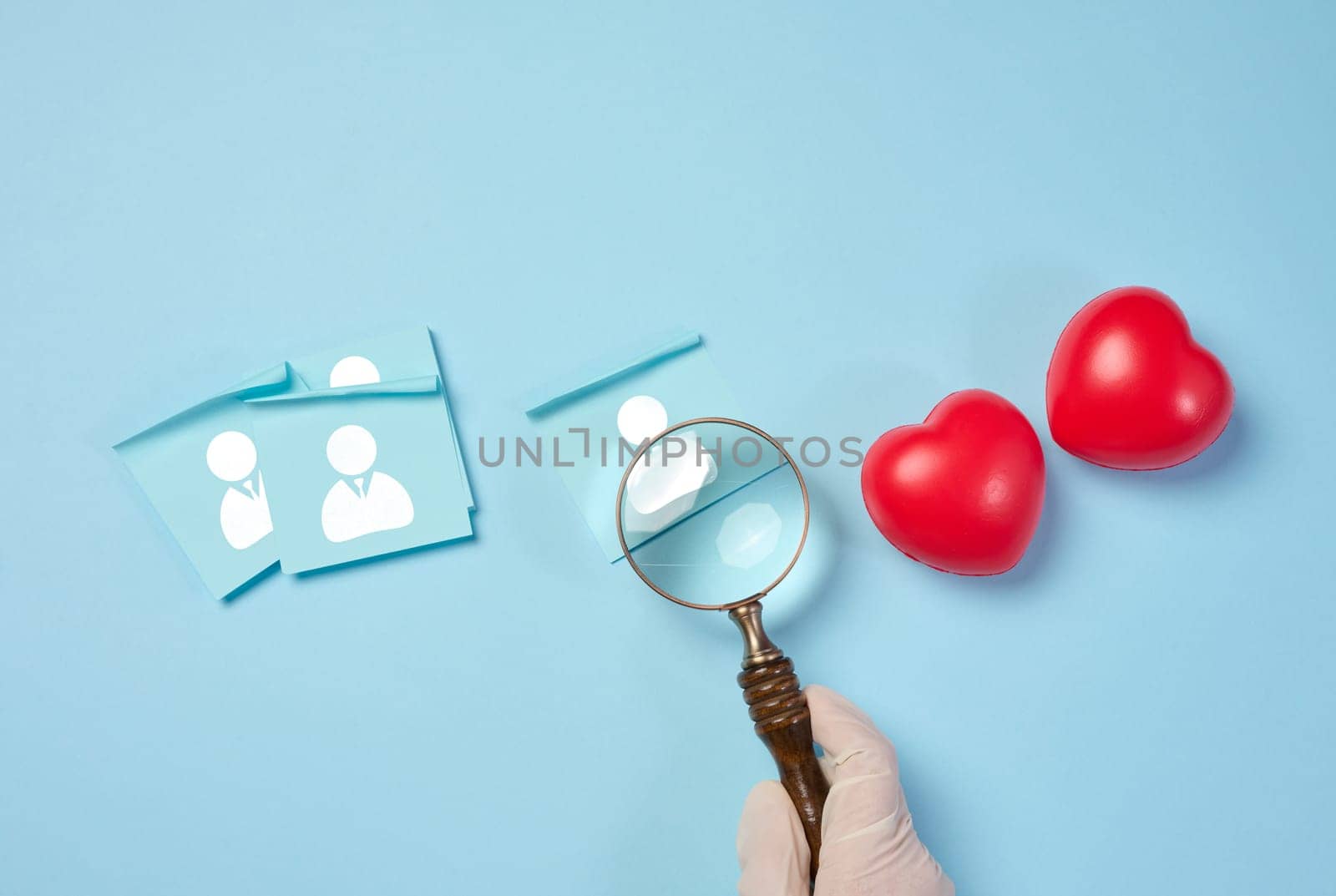 Female hand holding magnifying glass and red hearts on blue background, donor selection