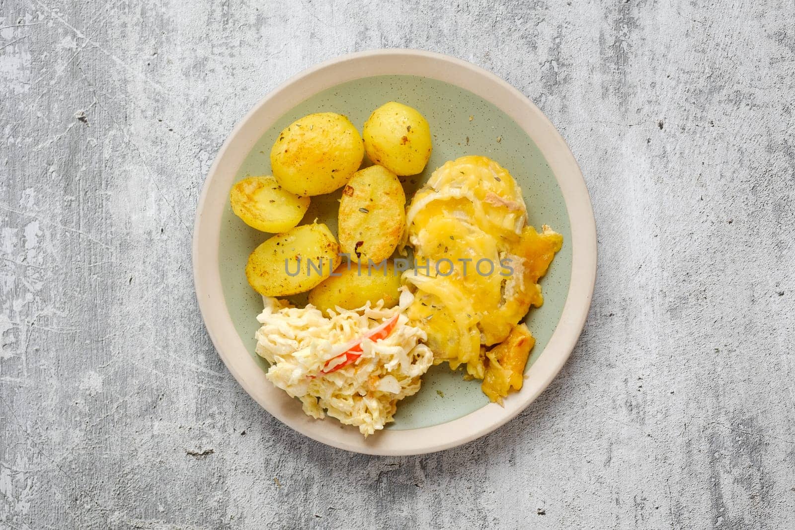 Overhead view of baked pork fillet with melted cheese and onion served with fried potato and cabbage salad