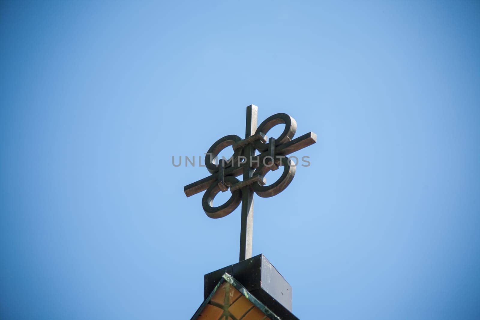 A unique metal cross on a top of building, featuring four interconnected circles at its center against a clear sky.