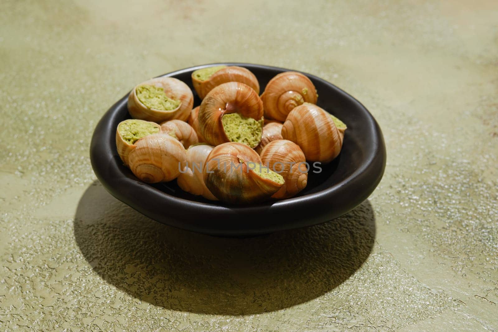 Edible snails Escargot stuffed with spicy herbal butter on green background