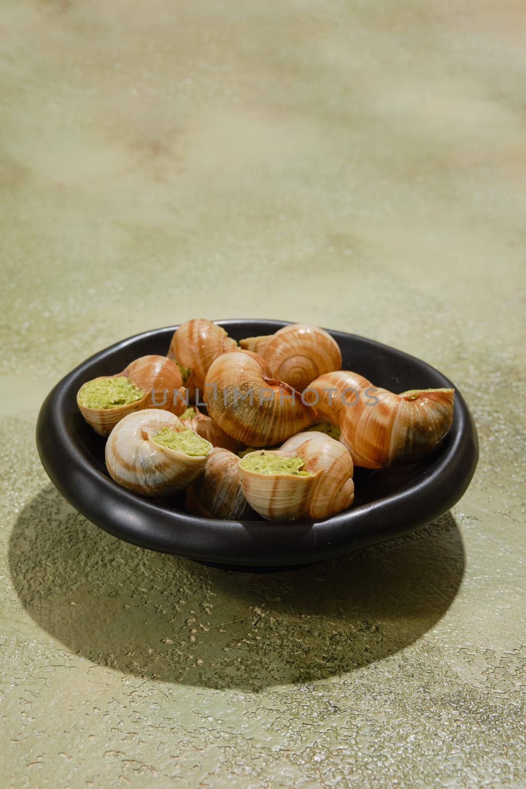 Black plate full of Escargot snails stuffed with spicy butter and cilantro