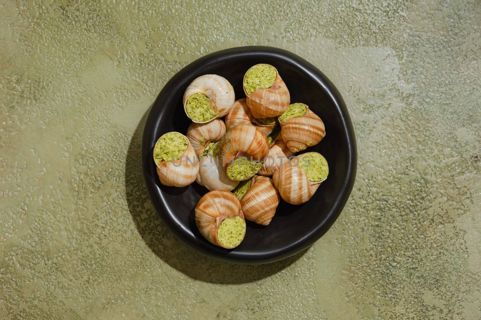 Overhead view of Edible snails stuffed with spicy herbal butter in black bowl
