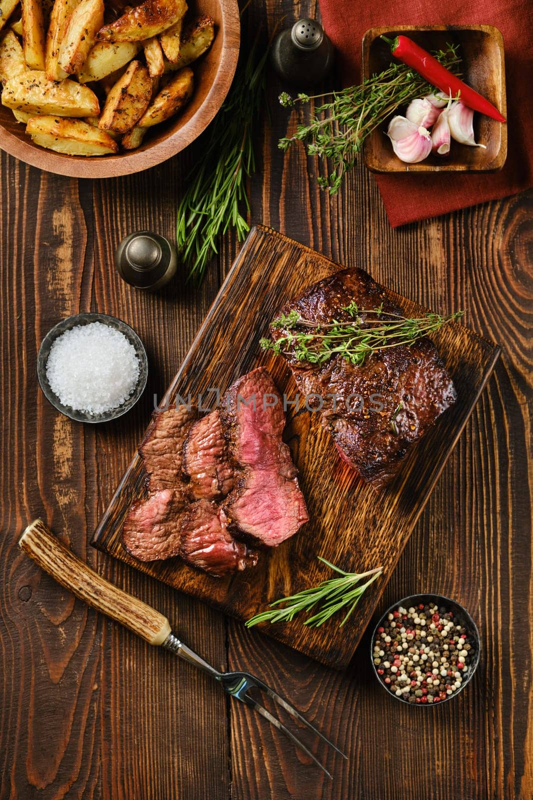 Overhead view of juicy grilled top blade beef steak on wooden cutting board with garnish