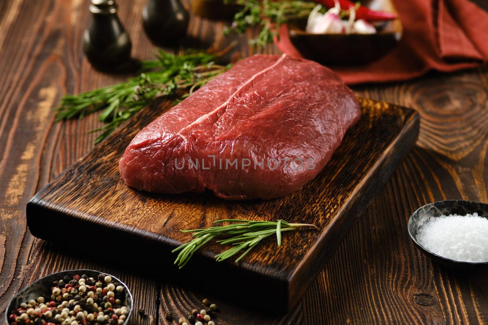 Raw top blade beef steak on wooden cutting board surrounded with spice and herbs