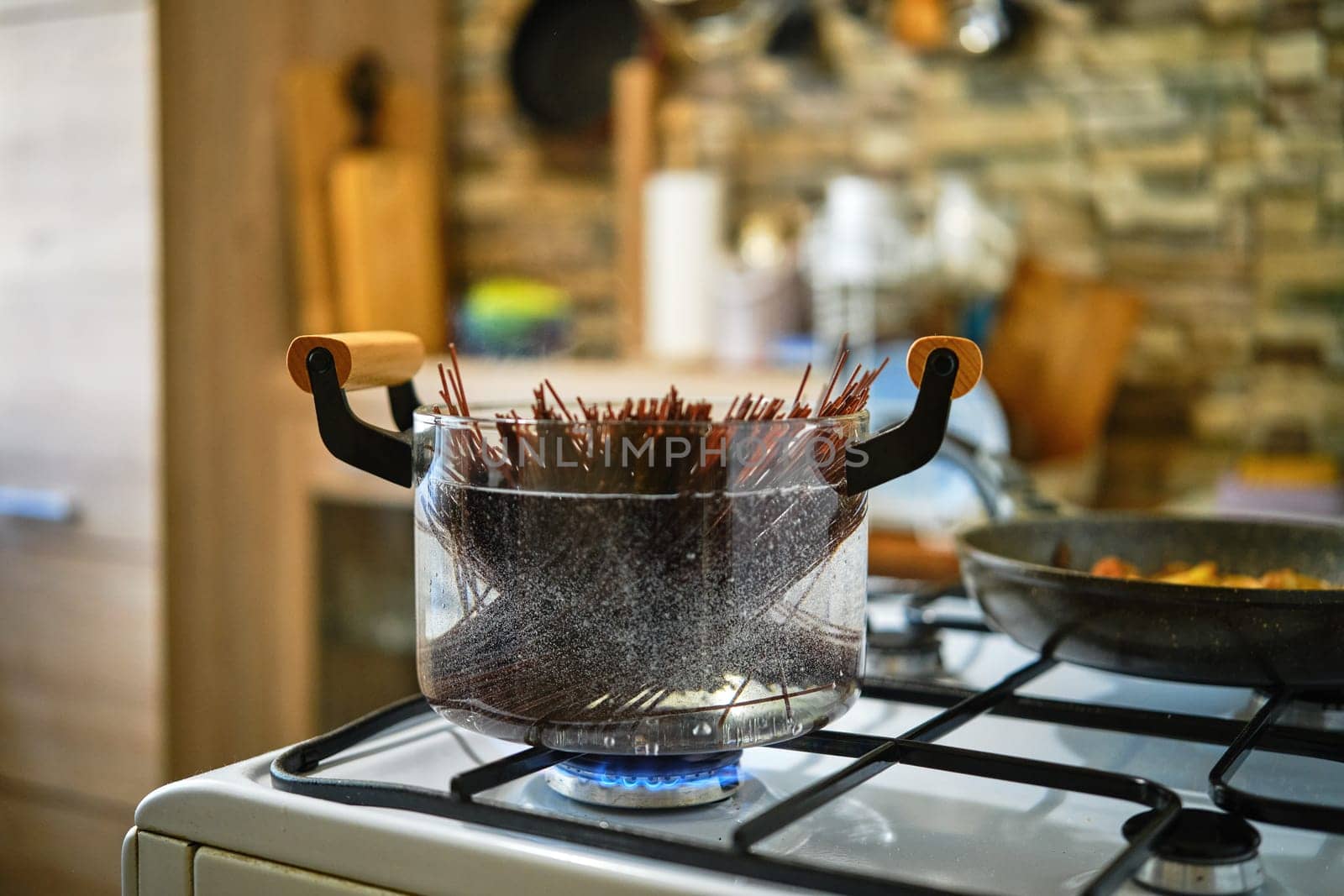 Cooking black rice noodles in transparent glass saucepan on a gas stove in the kitchen