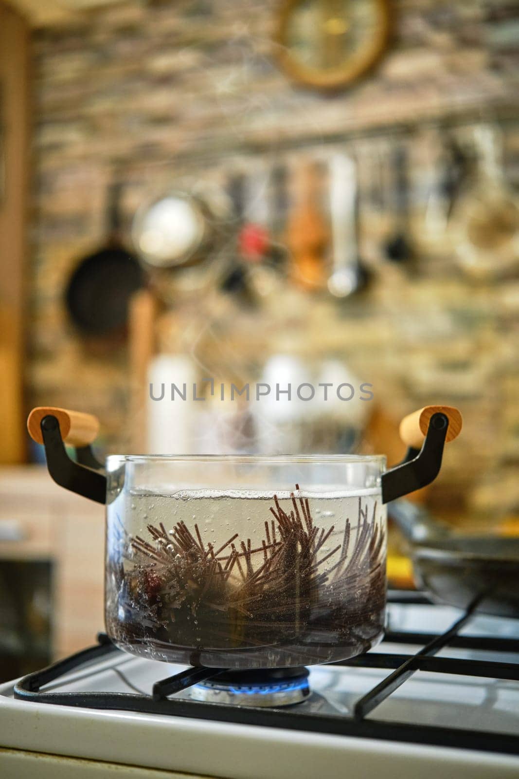Black rice noodles boiling in transparent glass saucepan on a gas stove